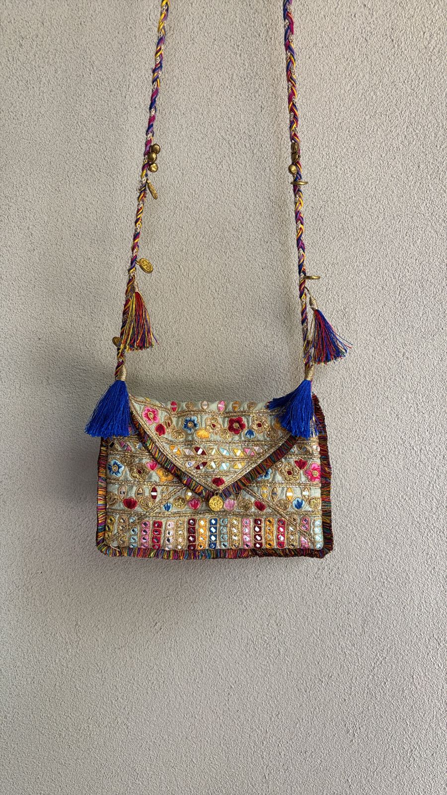 Green multicolored envelope sling bag with resham embroidery, mirror embellishments, braided dori strap, and vibrant tassel accents
