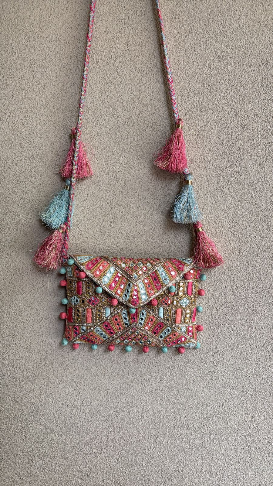 Multicolored envelope bag with thread, mirror work and tassel detailing on the sling